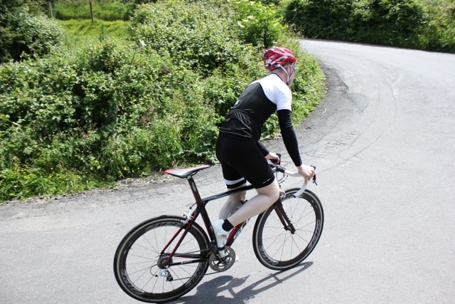 A cyclist rides in a black jersey with white shoulders and blacks shorts with a white stripe